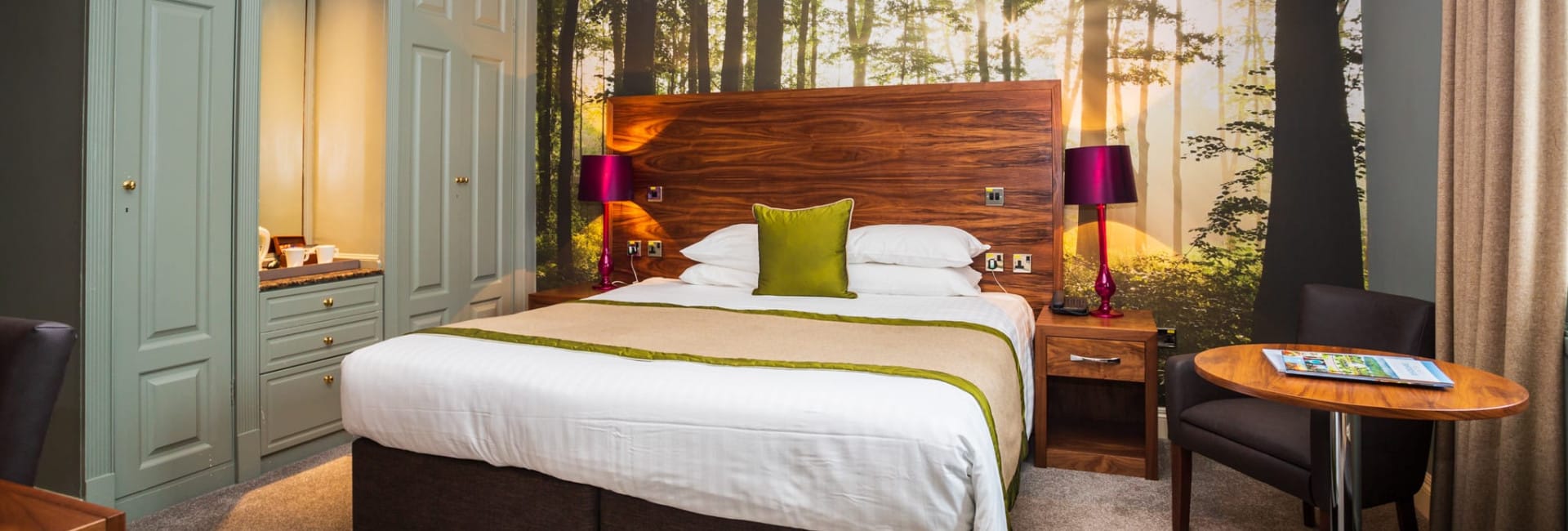 Superior double room at The Moat House featuring a king-size bed, forest-themed wall mural, modern furnishings, and soft ambient lighting.