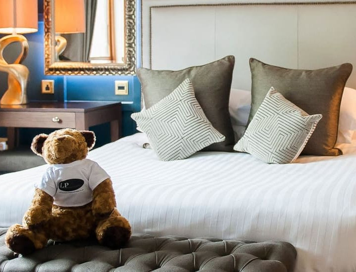 Plush bed at The Moat House with stylish cushions and a teddy bear wearing an LP shirt, representing The Lewis Partnership, owners of the Moat House.