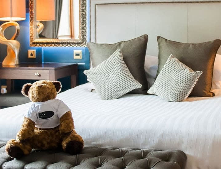Plush bed at The Moat House with stylish cushions and a teddy bear wearing an LP shirt, representing The Lewis Partnership, owners of the Moat House.