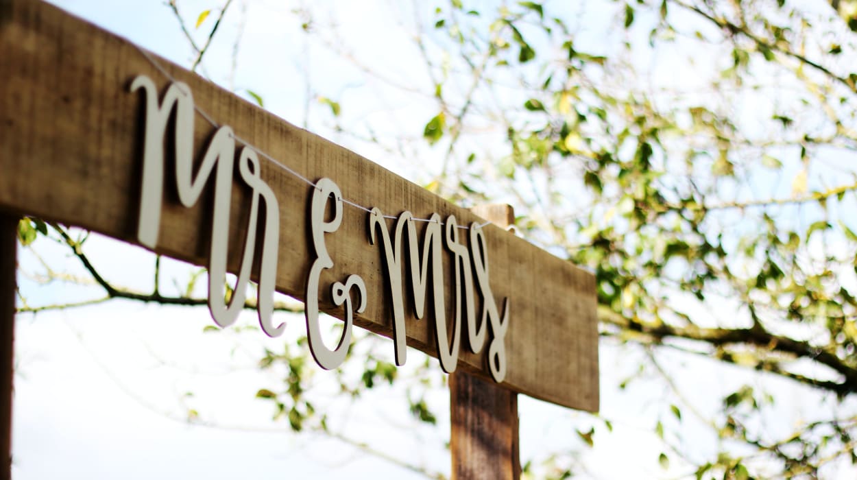 A rustic wooden wedding sign with white hanging letters spelling 